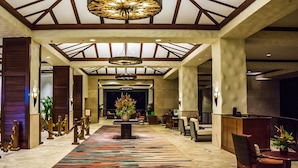 A hotel lobby with a central floral arrangement, a patterned carpet, and a high ceiling with wooden beams.