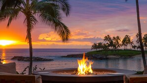 A fire pit with a view of the ocean and palm trees at sunset.