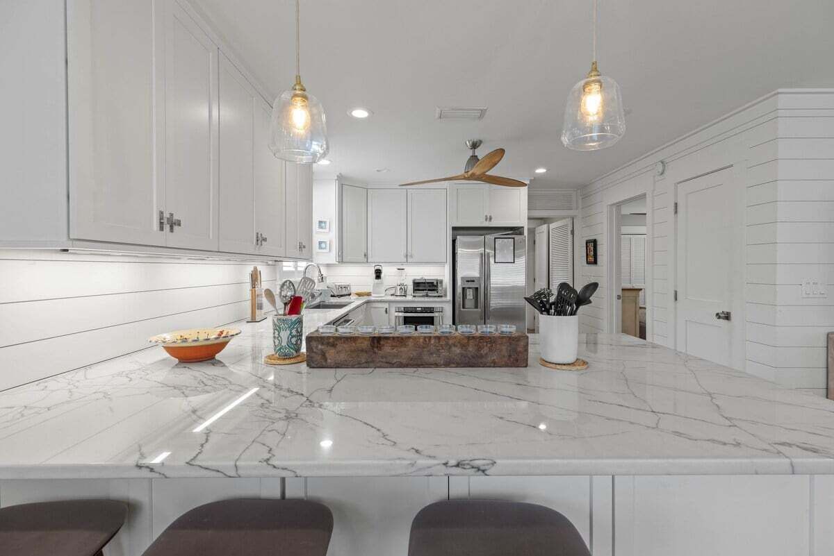 A modern kitchen with white cabinetry, a marble countertop, and pendant lighting.