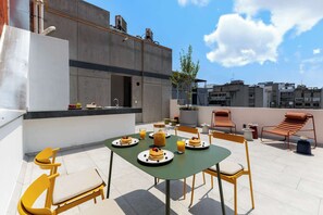 A rooftop terrace with a table set for breakfast, chairs, and a view of surrounding buildings.