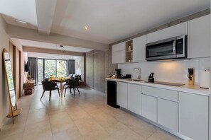 A modern kitchen with white cabinetry, a built-in microwave, and a dining area with a table and chairs.