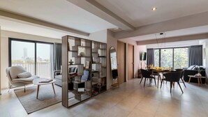 A spacious living area with a modern sofa, a dining table with chairs, a bookshelf, and a large window offering a city view. - Capitalia Hipódromo | Skyline Peace, Seamless Stay (Ciudad de México)