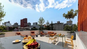 A rooftop terrace with outdoor seating, a dining table with fruits and a dessert, and a cityscape view in the background. - Capitalia Hipódromo | Skyline Peace, Seamless Stay (Ciudad de México)