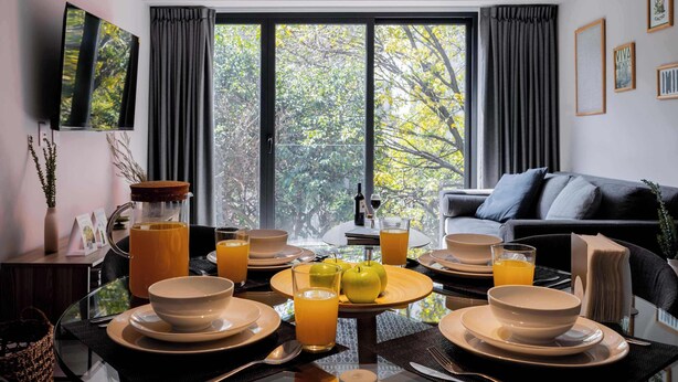 A dining area with a table set for breakfast, a sofa, and a TV mounted on the wall. - Capitalia Hipódromo | Skyline Peace, Seamless Stay (Ciudad de México)