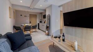 Un salon moderne comprenant un canapé, un coin repas, une cuisine et un téléviseur fixé au mur.