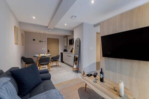 Un salon moderne comprenant un canapé, un coin repas, une cuisine et un téléviseur fixé au mur.