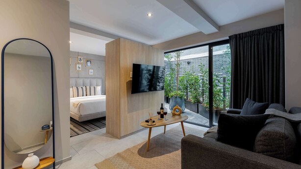 Une chambre d’hôtel moderne équipée d’un lit, d’une télévision, d’un canapé et d’un balcon agrémenté de plantes.