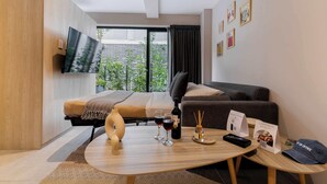 Une chambre d’hôtel moderne équipée d’un lit, d’un canapé, d’un téléviseur fixé au mur, d’une table basse avec des verres à vin, une bouteille et un bouchon.