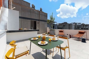 Une terrasse sur le toit, avec une table dressée pour le petit-déjeuner, des chaises et une vue sur les bâtiments environnants.
