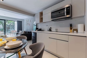 Une cuisine moderne dotée d’un four à micro-ondes encastré, d’un coin repas avec une table en verre et offrant une vue sur l’extérieur.