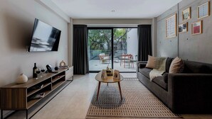 A modern living room with a flat-screen TV, a sofa, a coffee table, and a sliding glass door leading to an outdoor seating area. - Capitalia | Your Sky-High Sanctuary in Condesa (Ciudad de México)