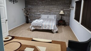 Un dormitorio con cama, mesita de noche, lámpara, un jarrón con flores y ventana con persianas.