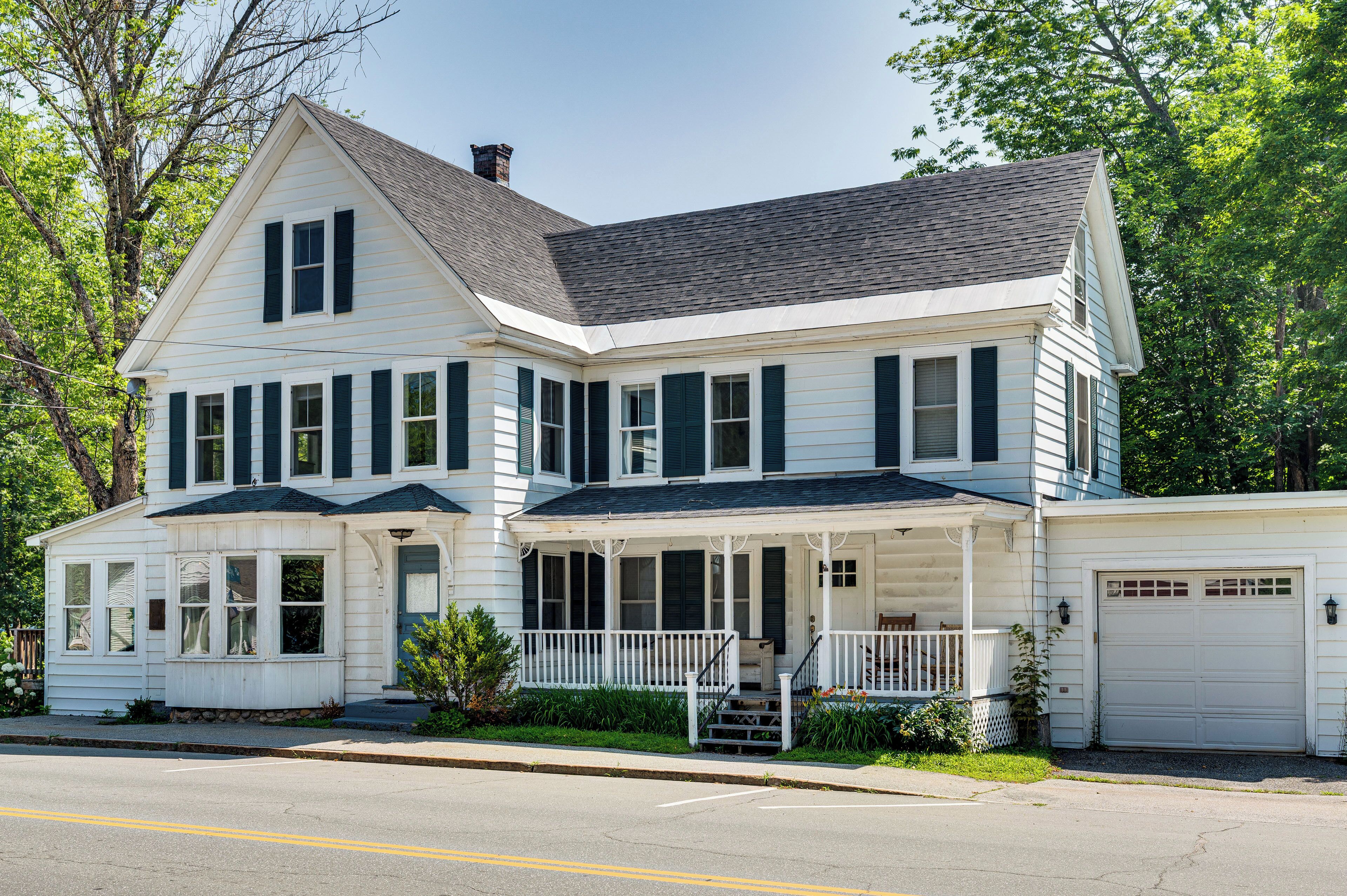 A two-story white house with dark shutters, a front porch, and a garage.