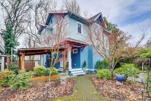 Une maison à deux étages, avec une façade bleue, un porche abrité et un jardin agrémenté de diverses plantes ainsi qu’un sentier.