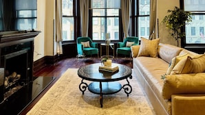 A living room with a fireplace, a sofa, a coffee table, and two green armchairs. - Gilded Age Gold Coast Mansion with Parking, Deck, Fireplaces (Chicago)