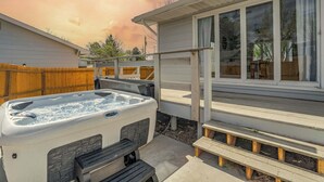 Un jacuzzi en un patio trasero con una terraza de madera y una casa al fondo.