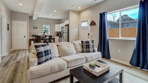 Ein modernes Wohnzimmer mit einem beigefarbenen Sofa, einem Couchtisch und einem großen Fenster mit Vorhängen.