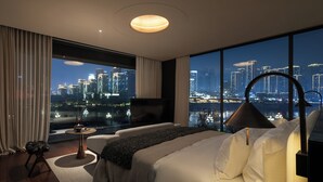 Una habitación de hotel moderna con un amplio ventanal que ofrece vistas a la ciudad, una cama, una zona de estar y un televisor.