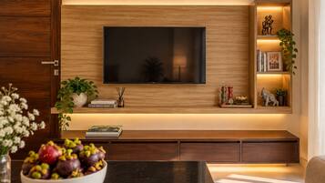 Una sala moderna con un televisor de pantalla plana montado en una pared de madera, una estantería con objetos decorativos y un frutero sobre una mesa.