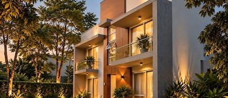 A modern two-story building with a balcony, large windows, and a well-maintained garden.