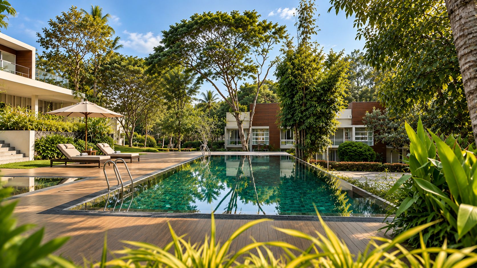 A swimming pool with lounge chairs and a wooden deck, surrounded by greenery and buildings.