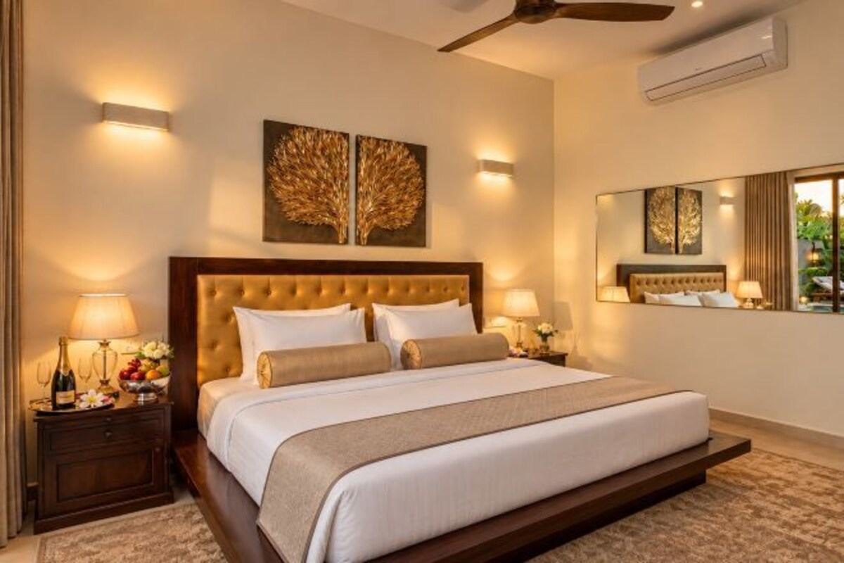 A hotel room with a large bed, two bedside tables with lamps, a ceiling fan, and a large mirror.