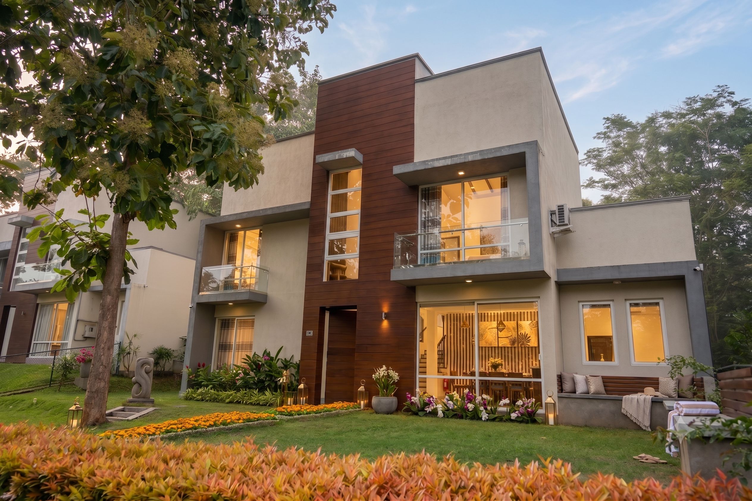 A modern two-story residential building with a balcony, large windows, and a well-maintained garden.