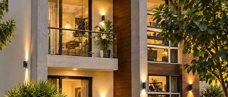 A modern two-story house with a balcony, large windows, and a well-lit garden.
