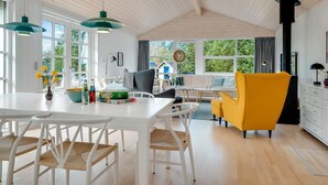 Une cuisine moderne avec des meubles blancs, une table à manger avec des chaises et un fauteuil jaune.