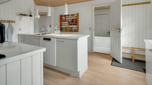 Une cuisine moderne avec des meubles blancs, un îlot central, des luminaires suspendus et un plafond en bois.