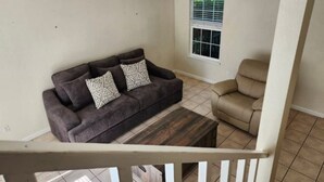 A living room with a dark brown sofa, two patterned cushions, a wooden coffee table, and a beige armchair.