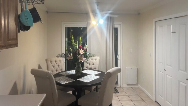 A dining area with a round table, four chairs, a vase with flowers, and a ceiling fan.