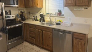 A kitchen with wooden cabinets, stainless steel appliances, a dishwasher, and a window with blinds.