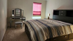 A bedroom with a bed, a desk, a chair, a dresser, and a window with a blind.
