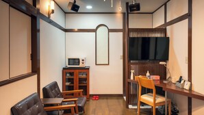 A room with a wooden desk, a television, a microwave, and a seating area with chairs and a sofa. - Grand Hotel Narita Airport (Narita)