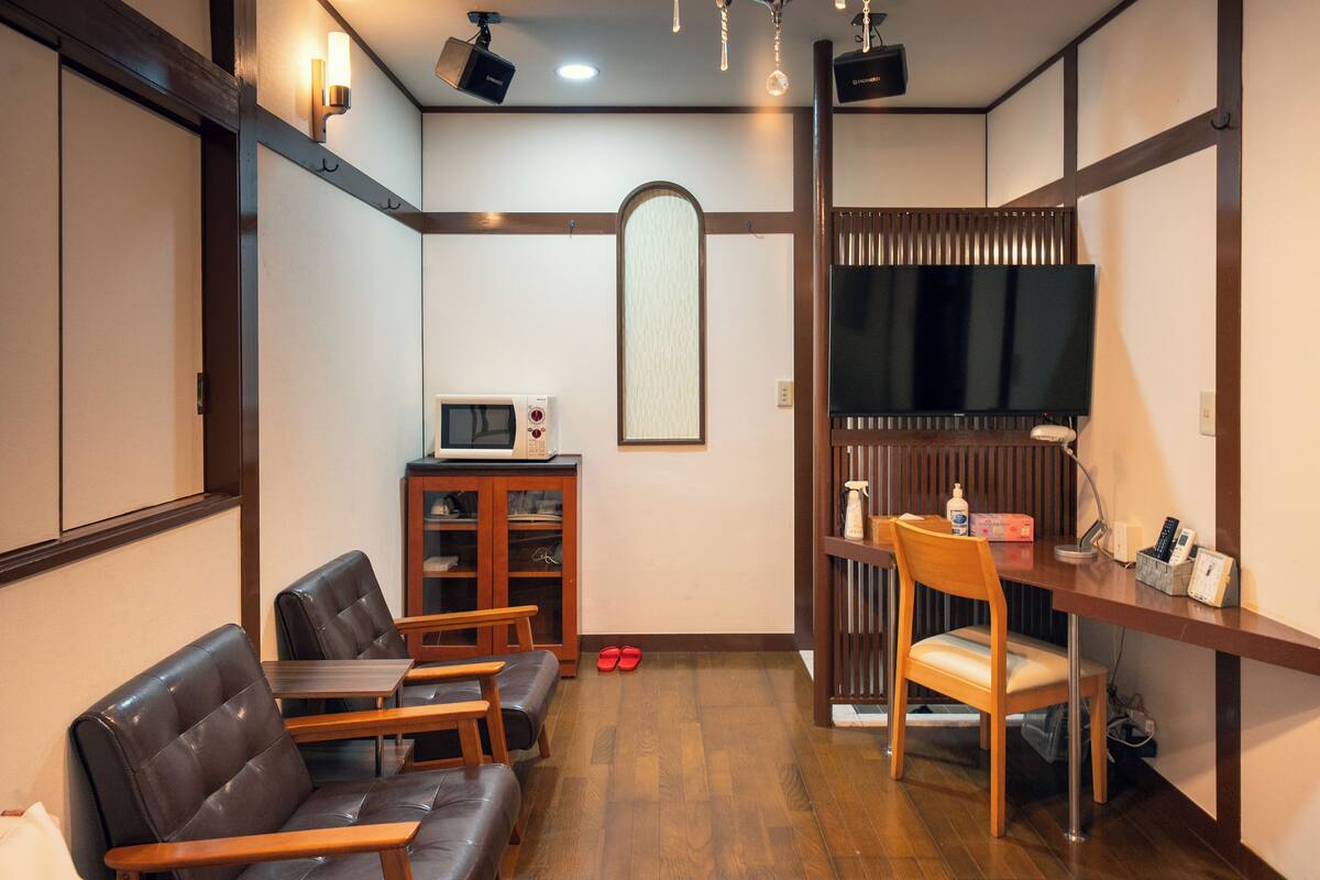A room with a wooden desk, a television, a microwave, and a seating area with chairs and a sofa.