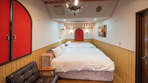Quarto de hotel com uma cama grande, uma porta vermelha, um banco de madeira e um ventilador de teto.