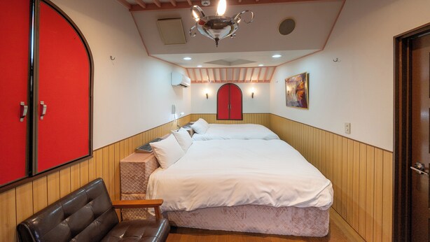A hotel room with a large bed, a red door, a wooden bench, and a ceiling fan. - Grand Hotel Narita Airport (Narita)