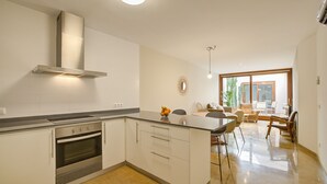 A modern kitchen with a central island, built-in oven, and stainless steel range hood. - Comtat Muro 1 by Renallorca (Muro)