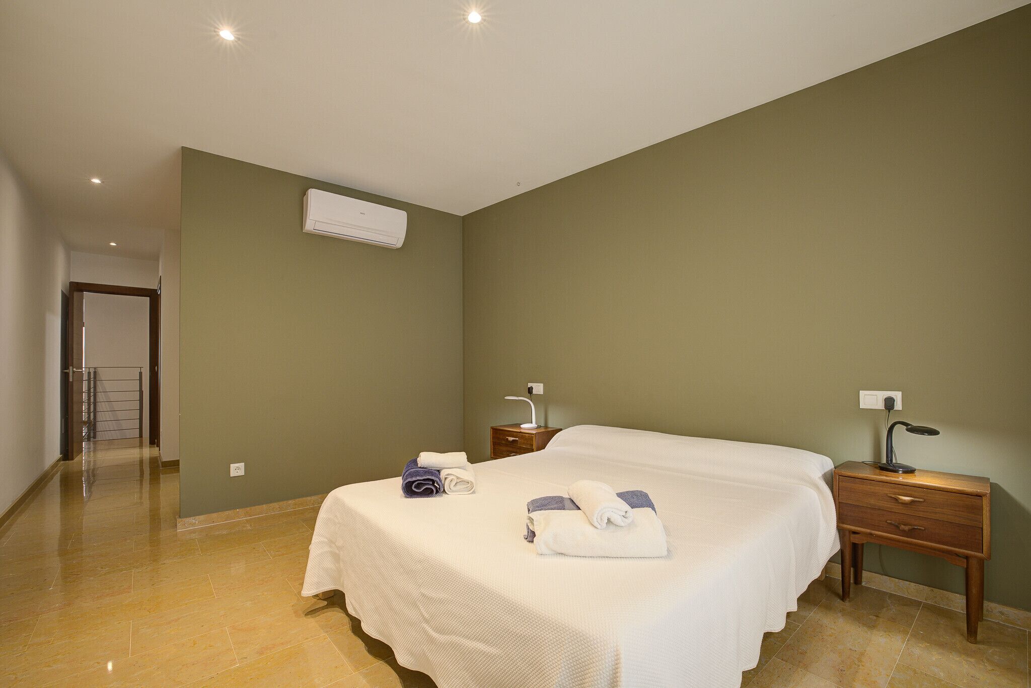 A bedroom with a bed, a nightstand, a bedside table, and an air conditioning unit.