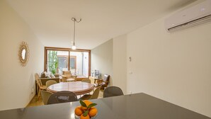 A dining area with a round table, chairs, and a bowl of oranges. There is a window with a view of greenery outside. - Comtat Muro 1 by Renallorca (Muro)