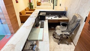 Un espace de bureau moderne avec un long comptoir d’accueil, un poste informatique et un coin salon.