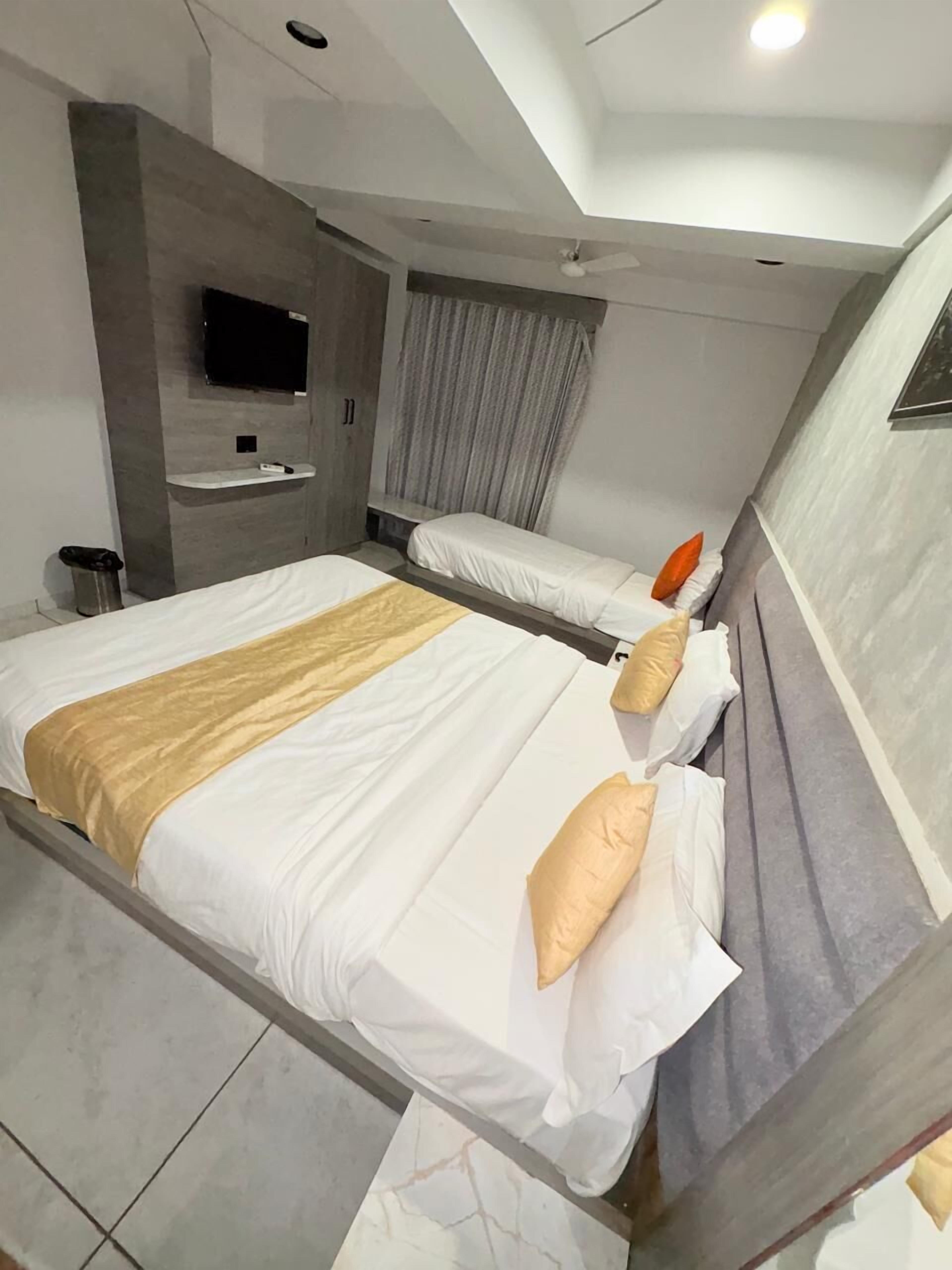 A modern hotel room with two beds, a flat-screen TV mounted on the wall, a small shelf, and a ceiling fan.