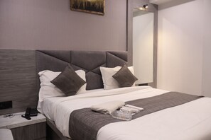 A modern hotel room with a large bed, a bedside table with a phone, and a mirror on the wall.