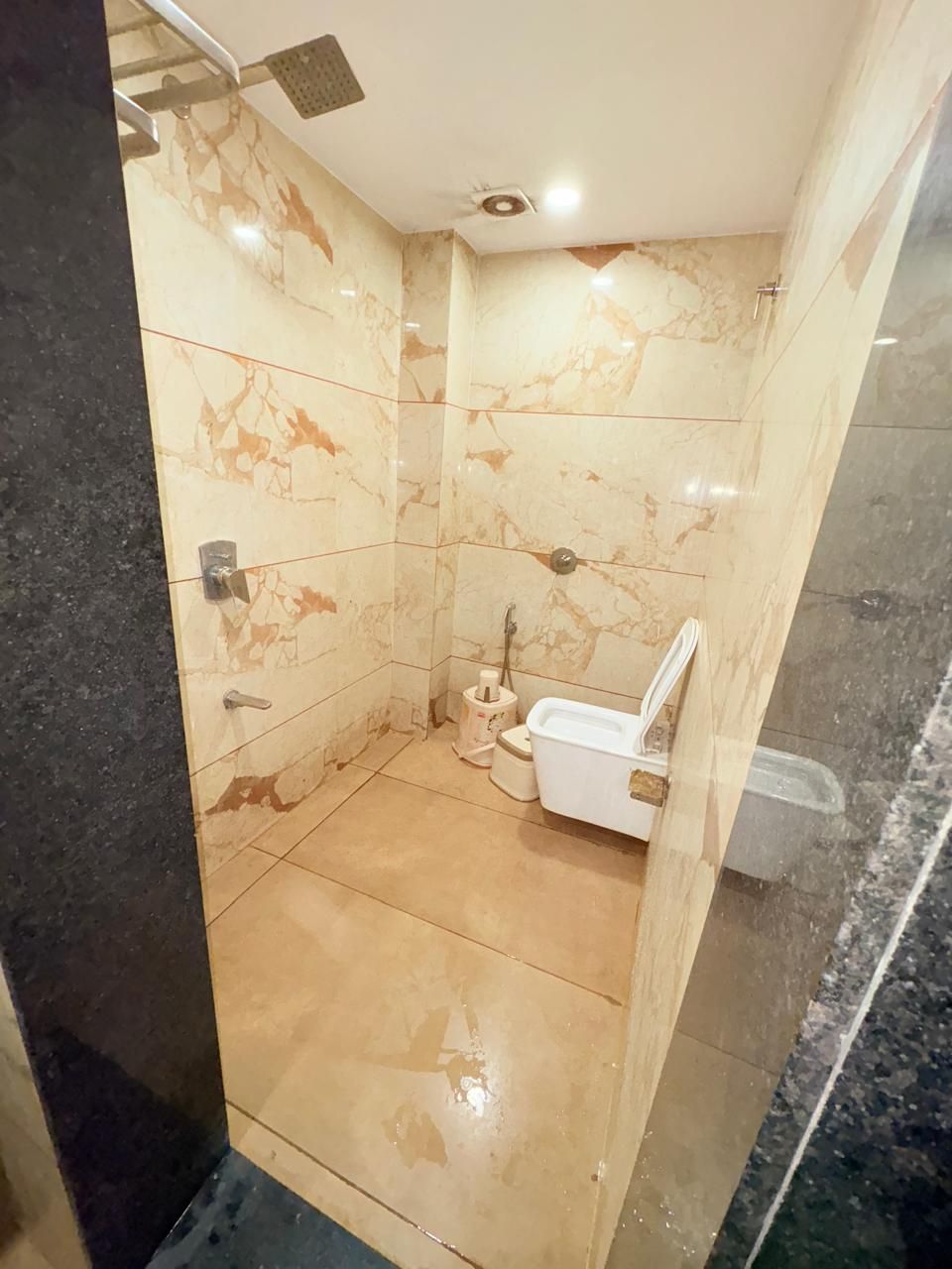 Un baño moderno con paredes y suelo de mármol, cabina de ducha con mampara de vidrio y un inodoro blanco.
