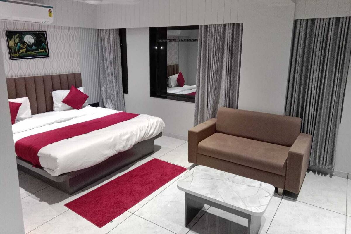 Una habitación de hotel moderna con una cama grande, un sofá, una mesita y un espejo.