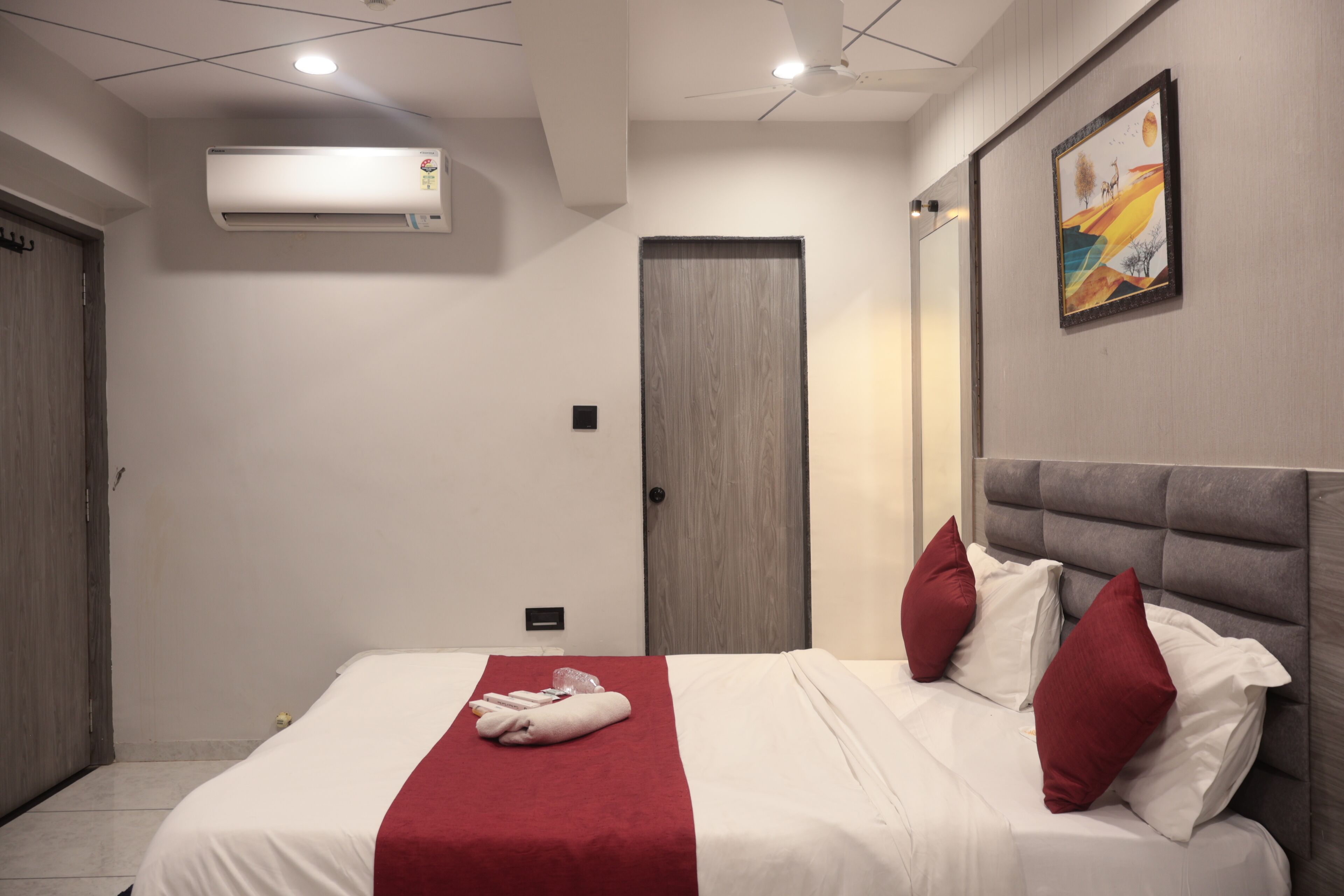 Quarto de hotel com uma cama, um cobertor vermelho e um quadro na parede.