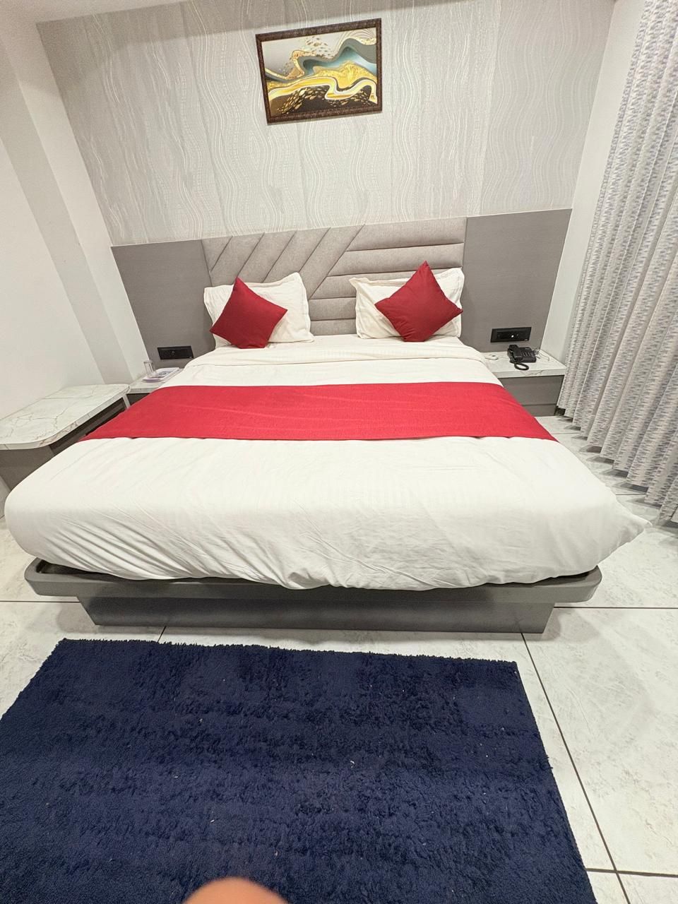 A modern hotel room with a large bed, a red and white bedspread, and a blue rug.