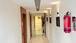 Un couloir d’hôtel avec un sol en marbre poli, une porte en bois sur la gauche et un extincteur sur la droite.
