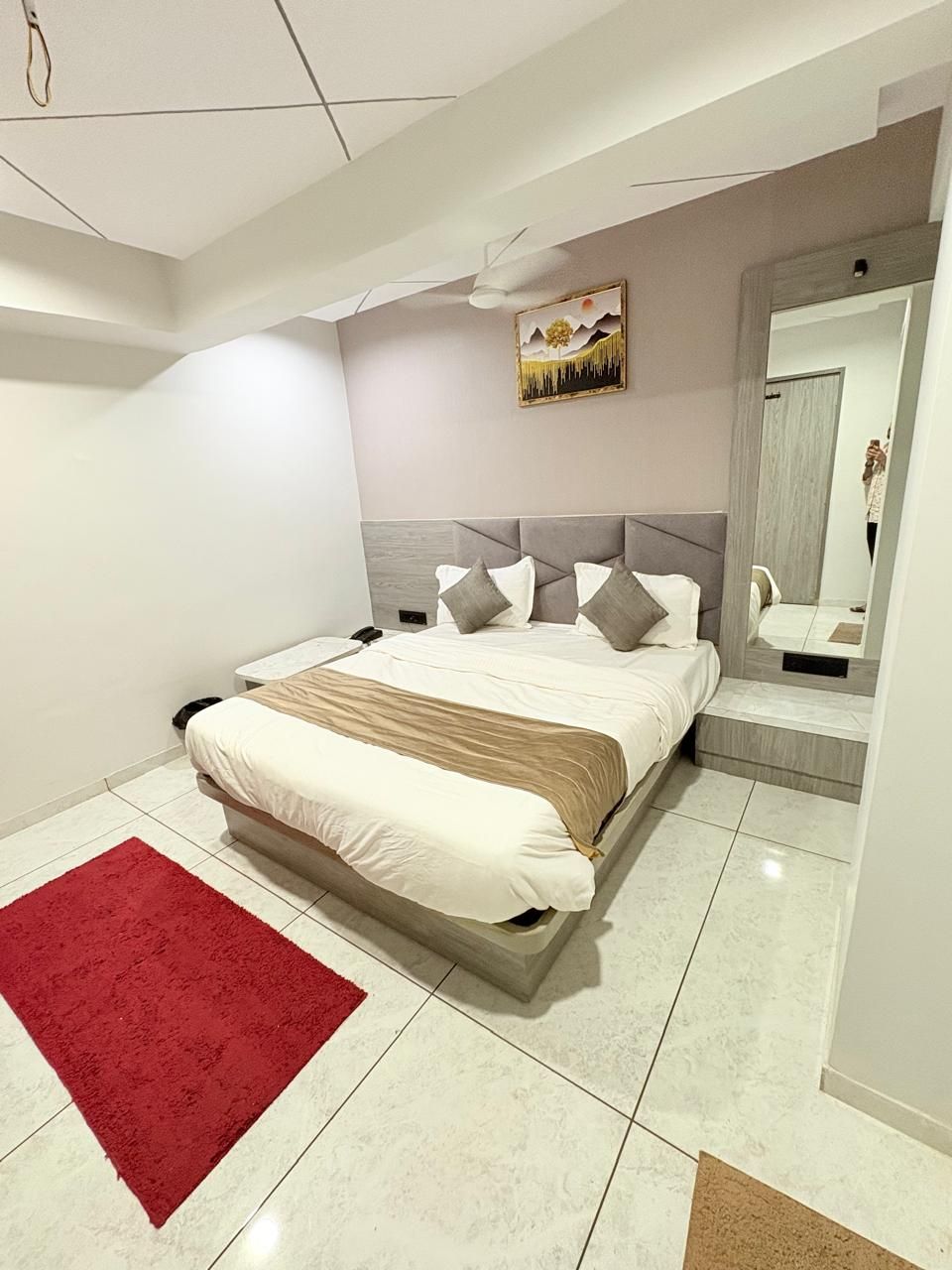 A modern bedroom with a bed, a red rug, a painting, and a mirror.